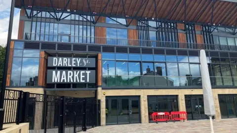 Entrance to a new market shows a stone building with black and grey windows and wood detailing