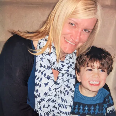 Rachel and her son Jonah both hugging and smiling. Rachel has light hair and blue eyes, Jonah has dark hair and brown eyes, they are both wearing blue tops.