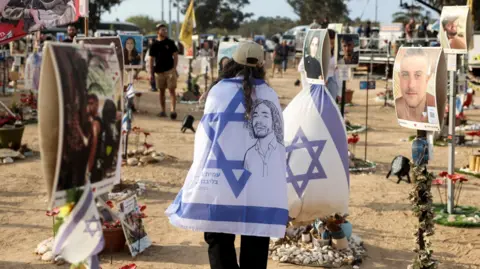 Reuters A woman walks wearing a cream baseball cap and an Israeli flag as people visit the site of the Nova festival