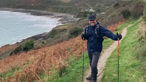 Tom Keys-Toyer, holding red polls on the side of trail next to the sea