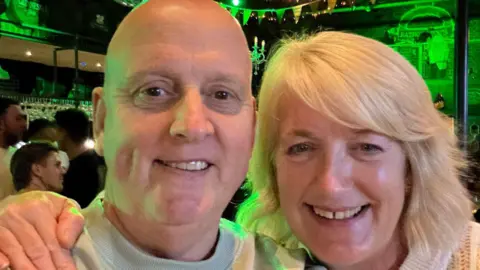 supplied A middle aged man and woman pose together, both smiling broadly.