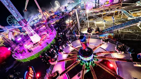 PA Media Colourful rides and a rollercoaster lit up against the night sky at Hull Fair.