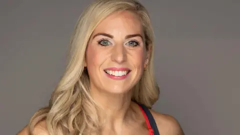 Melissa Power smiles at the camera. She had blonde hair and is wearing a sports vest. 
