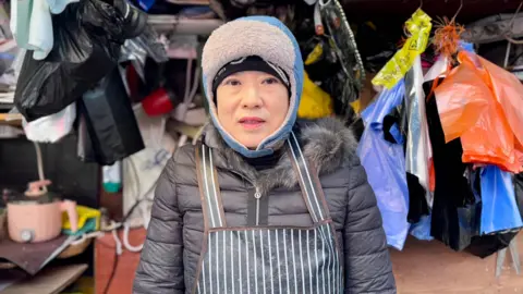 A woman wearing a winter hat and coat looks at the camera