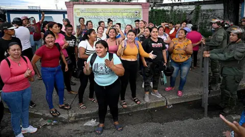 Federico PARRA / AFP via Getty Images Relatives of prisoners demand information about the transfers at the Internado Judicial Barinas (Injuba) prison in Barinas, Venezuela on May 25, 2026.
The group is mostly made up of women, they are gesticulating as members of the National Guard watch on. 