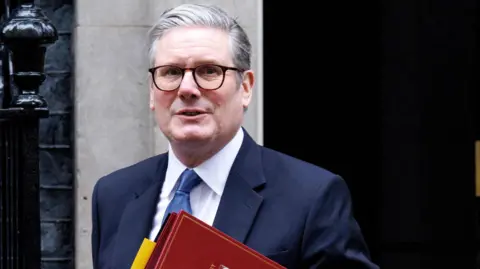 Sir Keir Starmer outside Downing Street - he is wearing glasses, a blue suit, white shirt and light blue tie and is carrying a red folder