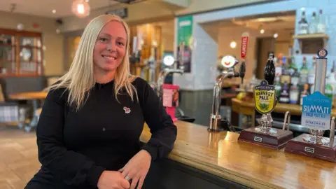 BBC Landlady Beccy Webster sitting in front of the bar of the pub