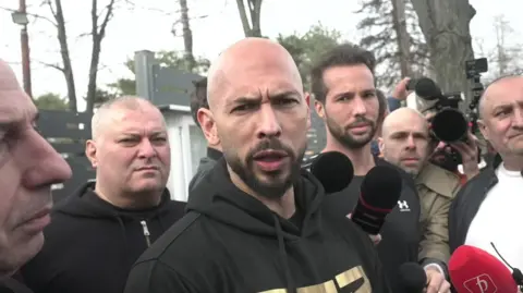 Andrew Tate with Tristan in background speaking outside a police station in Bucharest on 24/03/25