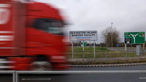 Getty Images A general view of the Sevington Inland Border Facility sign. There is a large red truck driving past.