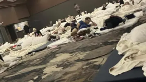 Nikki Finlay-Mulligan A conference room with lots of people on mattresses on the floor.