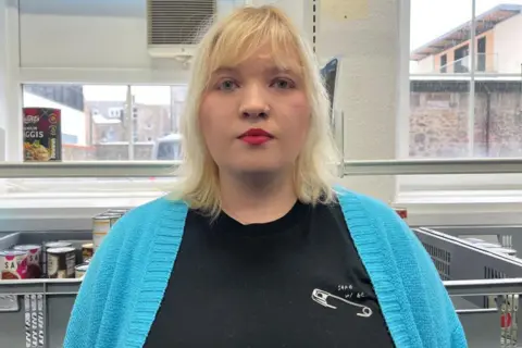 Eilidh MacKinnon looking at the camera, she has shoulder-length blonde hair and is wearing a bright blue cardigan over a black top.