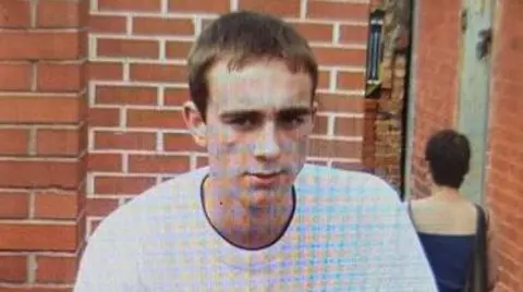 A grainy photo of a young man with shirt hair and wearing a white t-shirt. 