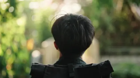 Getty Images The back of a young man/boy's head. He is either sitting or walking, but has a black rucksack on his back.