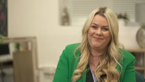 Carry sits inside the house with a neutral background smiling with long golden hair in a bright green jacket.