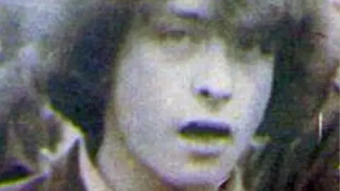 An aged photograph showing Kevin McKee. His is pictured looking to camera with long bushy hair covering his left eye.