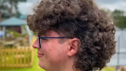 Teenage man with a large mullet of dark curly hair