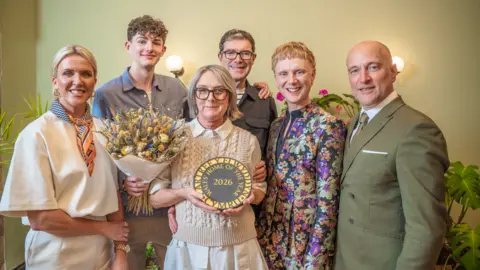 A group of women and men smiling and stood together with one woman holding an award that says 'Wales Home of the Year 2026'.