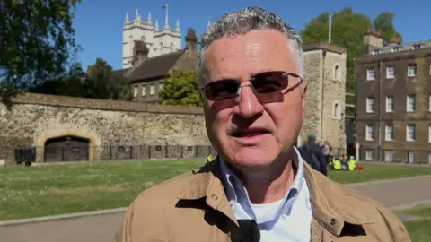 David Drew gives a TV interview in a street. He has short, grey hair and sunglasses.