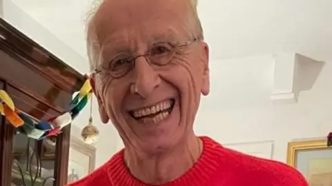 A man in a red Christmas jumper with a smile and glasses