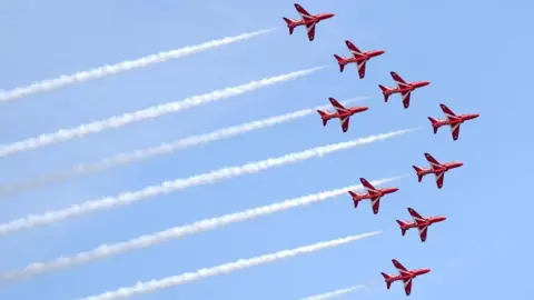 PA Media The Red Arrows fly in formation with a white vapour trail 