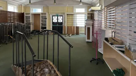 Ben Parker/BBC An empty shop with shelves along the walls, in the middle of the image is a walkway with rocks embedded on it to test walking shoes. 