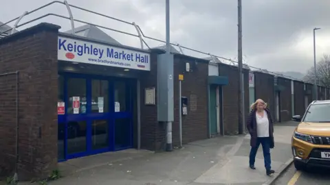 Blue metal doors in the entrance to a brown brick one-storey building with a sign above saying Keighley Market Hall 