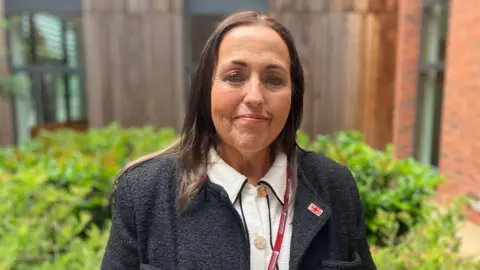 A woman stood outside a building wearing a Worcestershire County Council lanyard, a black jumper and a white shirt.