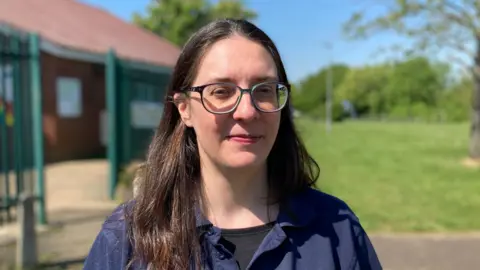 Headshot of Charis standing outside with the community centre in the background and a grassy field.