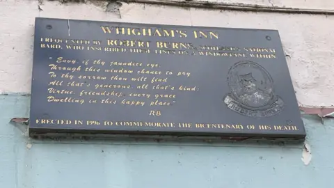 A plaque on the side of a building celebrating Robert Burns visits to the Whigham Inn and the poem he wrote about the site