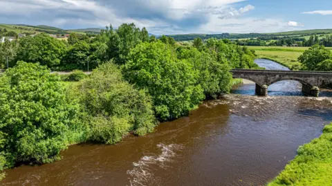 Fine & Country Scotland An aerial view of the River Nith with a bridge over it and trees overhanging into the water