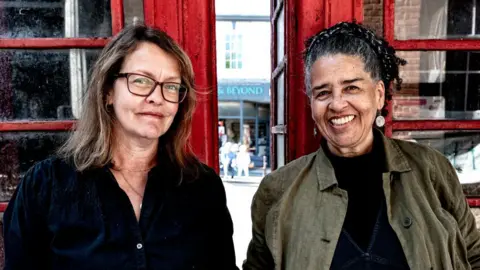 Lisa Wilson and Kim Squirrell smiling for the camera in front of the red phone boxes