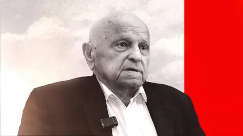 An elderly bald man in a suit looks off to the side of the camera