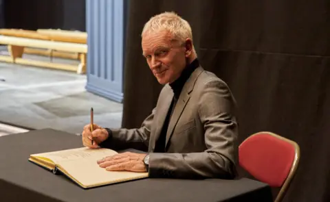 North Tyneside Council Sting smiling, in grey suit signing book