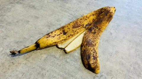 A yellow and brown banana skin waits on a floor
