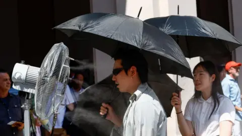 Reuters A man stands in front of a cooler spraying water ahead of Thom Browne’s Spring/Summer 2027 men’s collection show as part of Milan Fashion Week, in Mila
