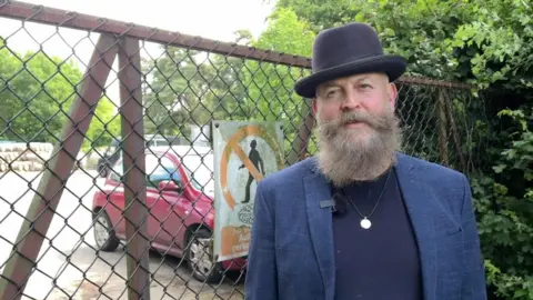 A middleaged man with a grey beard wearing a blue hat