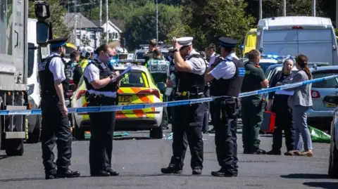 police officers standing in front of a line of cars and police tape