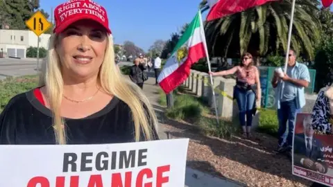 Bita Ashrafi wears a pro-Trump red cap and hols a sign saying "regime change"