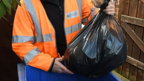 A black plastic bag above a blue recycling bin