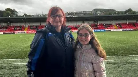 Institute / Emma Doherty Emma Doherty pictured with her daughter Ellen. 
She is wearing an Institute coat and her daughter is wearing a silver coat. 
They are both wearing glasses and have long hair.