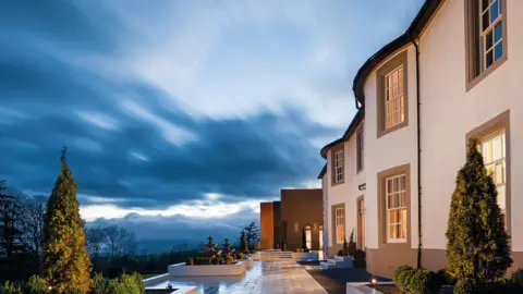 A picture of Hetland Hall Hotel viewed from the side with a dramatic sky above it