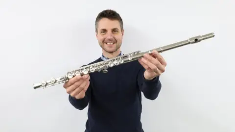 Gardiner Houlgate Auction House A man wearing a black jumper holds up a silver flute
