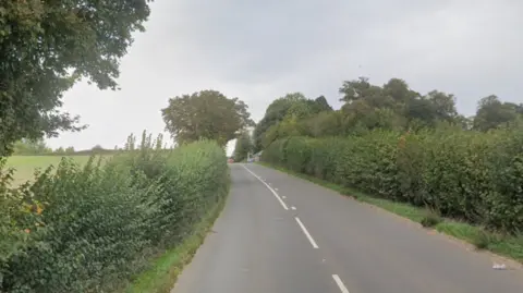 An empty country road with hedges and trees on either side