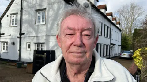 A man stands in front of some white houses.