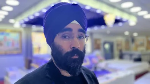 Kartar Singh Bring with a dark beard and glasses. He is wearing a purple turban.