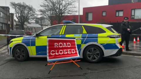 Road closed sign and police car and an officer standing next to the car.