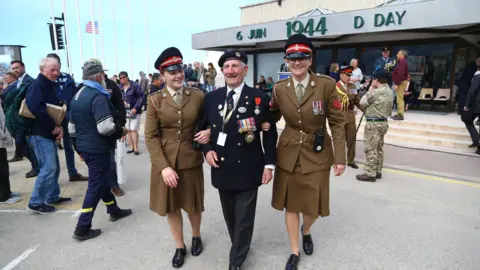 PA Media George Chandler leaving following a service in Arromanches, France, commemorating the 75th anniversary of the D-Day landings, supported by two members of the Women's Royal Army Corp.