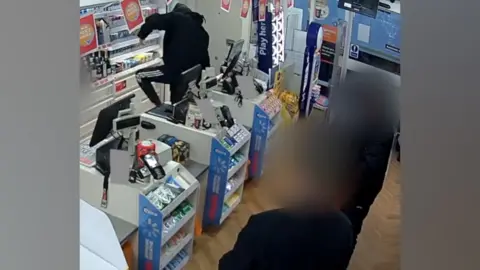 A man dressed in black climbing over a supermarket counter