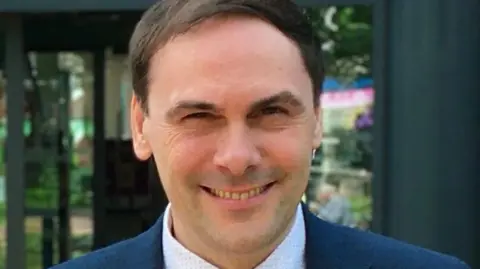 A man in a navy suit smiling at the camera.