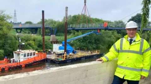 Worcestershire County Council Jon Fraser in a hi-vis jacket and hard white hat standing in front of the construction site of Kepax bridge